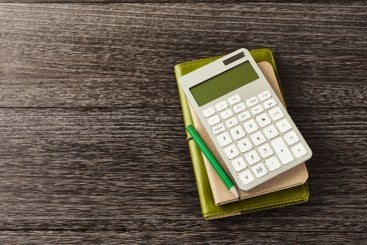 calculator on green notebook with green pencil on wooden table